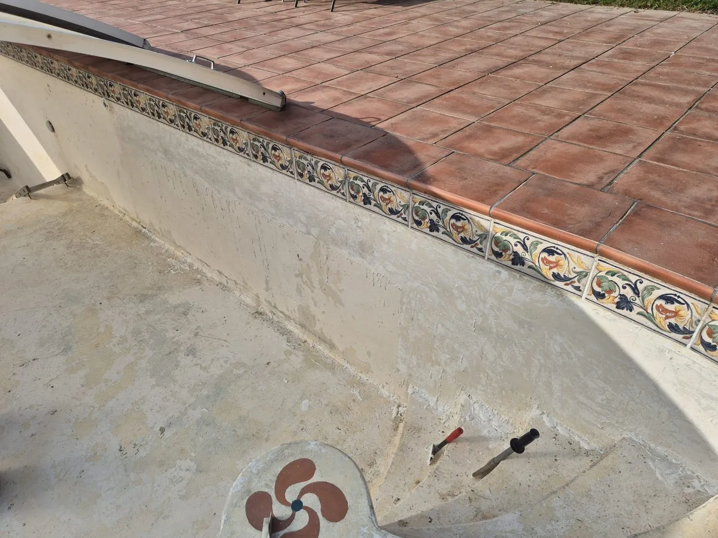 Bord d'un bassin de piscine vidé, paroi abîmée sous la margelle carrelée