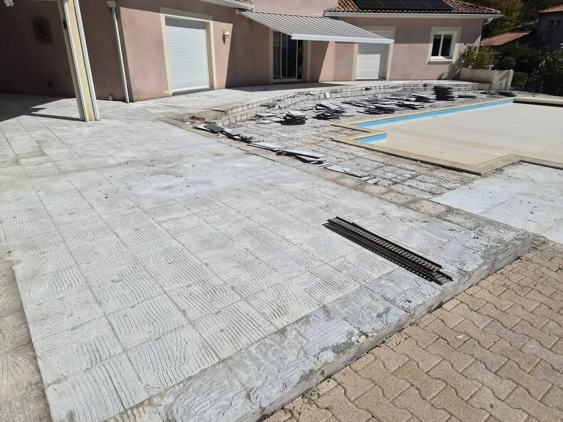 Terrasse de piscine dont l'ancien carrelage a été déposé, avec le support à nu et un caniveau