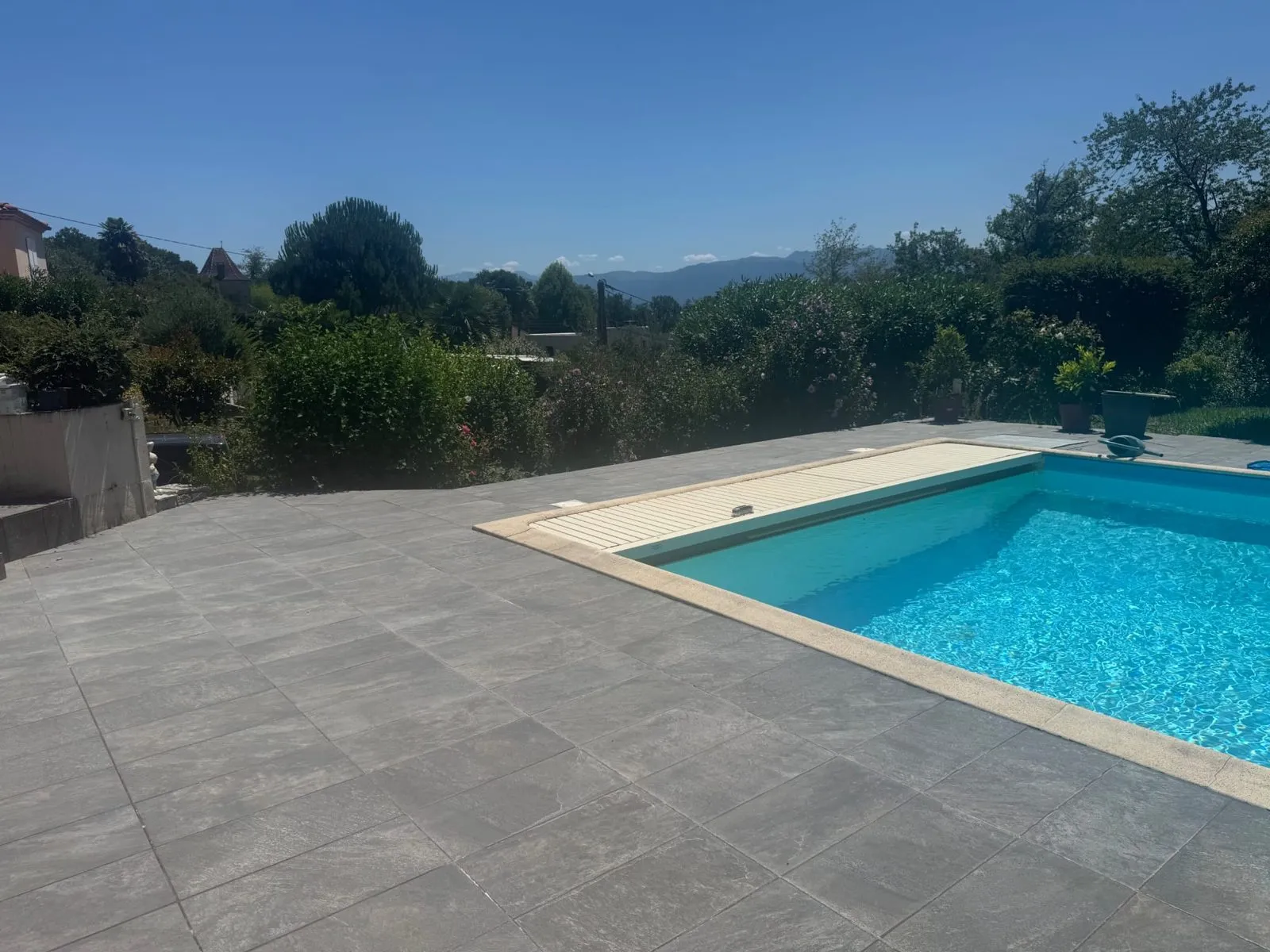 Terrasse carrelée en gris au bord d'une piscine, avec vue sur les collines