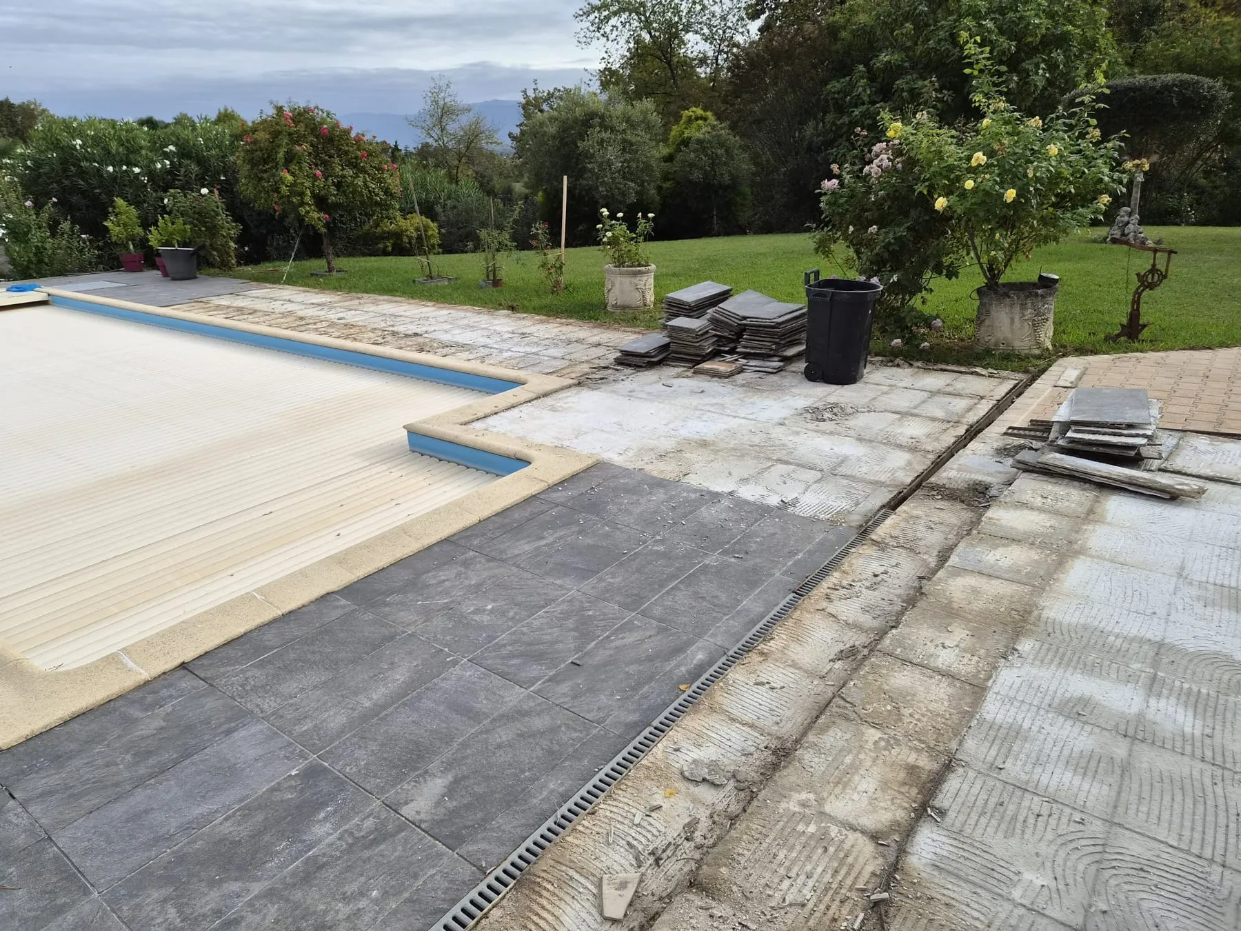 Terrasse de piscine en cours de pose, nouveau carrelage gris foncé à gauche et support à nu à droite